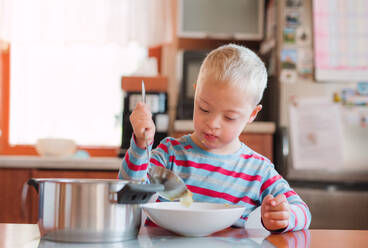 Ein behindertes Kind mit Down-Syndrom schüttet vor dem Mittagessen im Haus Suppe in einen Teller. - HPIF29860