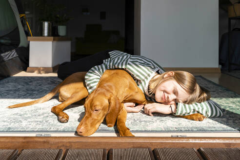 Smiling girl with Vizsla dog relaxing in sunlight at home - NDEF00633