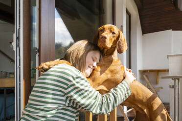 Smiling girl embracing Vizsla dog at home - NDEF00634