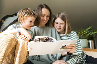 Lächelnde Mutter, die ihr Fotoalbum mit ihren Kindern zu Hause teilt - NDEF00646