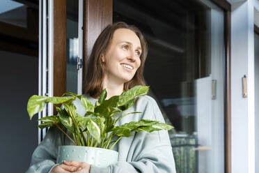 Smiling woman holding potted plant by door - NDEF00668