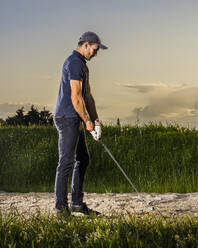 Mann bereitet sich auf einen Schlag beim Golfspielen in der Abenddämmerung vor - STSF03720
