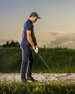 Man preparing to take shot playing golf at dusk - STSF03720