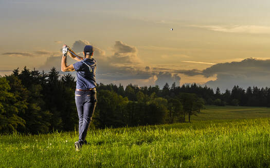 Junger Mann spielt Golf in der Abenddämmerung im Gras stehend - STSF03722