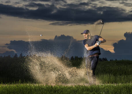 Man hitting golf ball at dusk - STSF03726