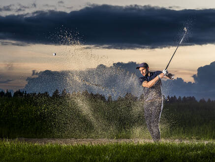 Man playing golf with club sanding on grass at dusk - STSF03727