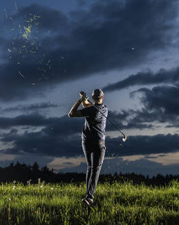 Mann spielt Golf im Gras stehend mit Blick zum Himmel in der Abenddämmerung - STSF03729
