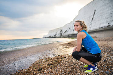 Young sporty woman runner with earphones resting outside on the beach in nature, listening to music. Copy space. - HPIF29890