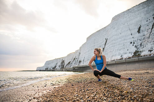 Junge sportliche Läuferin in blauer Sportkleidung, die sich draußen am Strand in der Natur streckt. Kopierraum. - HPIF29895