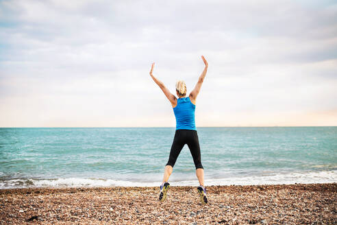Junge sportliche Läuferin in blauer Sportkleidung, die draußen am Strand in der Natur springt, Rückansicht. - HPIF29900