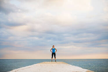 Eine junge, sportliche Frau, die auf einem Pier steht, draußen am Meer. Kopierraum. - HPIF29908