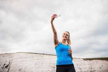 Eine fitte Läuferin macht ein Selfie am Strand mit ihrem Smartphone und Kopfhörern und lässt dabei Platz für Text - HPIF29914