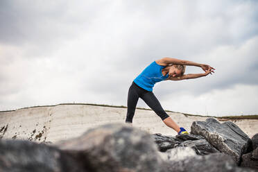 Junge sportliche Frau Läuferin mit Kopfhörer stehen draußen auf den Felsen am Strand in der Natur, Musik hören und Stretching. - HPIF29917