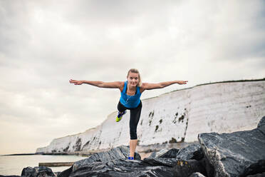 Young sporty woman runner with earphones stretching outside on the beach in nature. Copy space. - HPIF29921