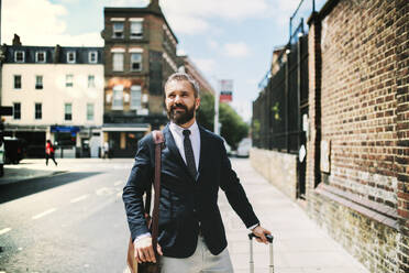 Hipster businessman with laptop bag and suitcase walking down the street in London. Copy space. - HPIF29924