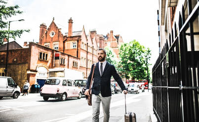 Hipster businessman with laptop bag and suitcase walking down the street in London. Copy space. - HPIF29925