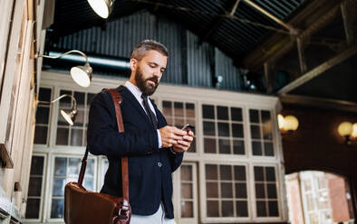 Ein Porträt eines Geschäftsmannes mit Smartphone, der in der Stadt steht und Textnachrichten schreibt. - HPIF29929
