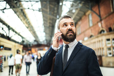 Zufriedener Geschäftsmann mit Smartphone auf der Londoner U-Bahn-Station Trian, der ein Telefongespräch führt. - HPIF29930