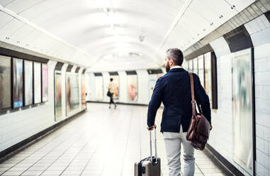 Rückansicht eines Geschäftsmannes mit einer Tasche und einem Koffer, der in der U-Bahn läuft. - HPIF29940