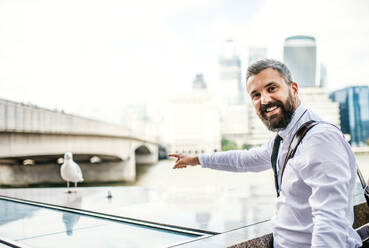 A hipster businessman standing by the river in London, pointing at seagull. - HPIF29953