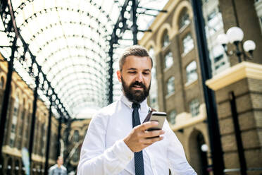 Glücklicher Geschäftsmann mit Smartphone auf der Trian-Station in London, Textnachrichten. - HPIF29958
