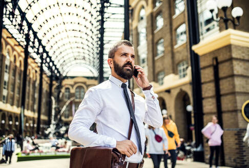 Happy businessman with smartphone on the trian station in London, making a phone call. - HPIF29959