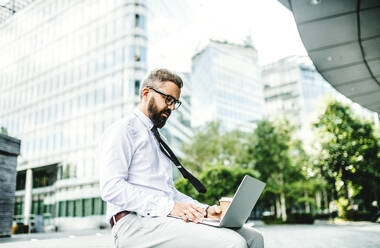 Hipster-Geschäftsmann mit Laptop sitzt im Freien auf der Straße in der Stadt. - HPIF29965