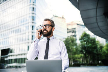 Hipster-Geschäftsmann mit Laptop und Smartphone in der Stadt, der ein Telefonat führt. - HPIF29967