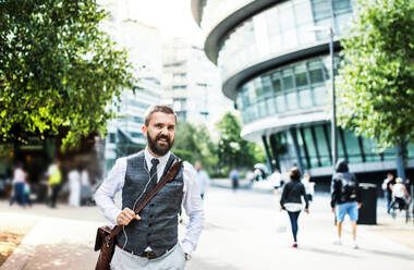 Hipster businessman with a bag and earphones walking on the street in London. - HPIF29973