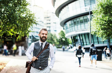 Hipster-Geschäftsmann mit einer Tasche und Kopfhörern auf der Straße in London. - HPIF29973