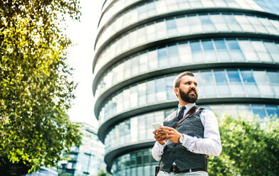 Low-Winkel-Porträt von Geschäftsmann mit Smartphone stehen auf der Straße in der Stadt vor einem Gebäude, Text-Messaging. - HPIF29974