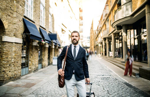 Hipster businessman with laptop bag and suitcase walking down the street in London. Copy space. - HPIF29991