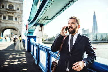 Hipster Geschäftsmann mit Smartphone steht auf der Brücke in der Londoner Stadt, einen Anruf tätigen. - HPIF29993