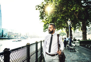 Serious hipster businessman with laptop bag walking by the river in London. - HPIF29998