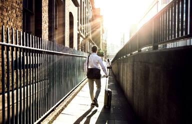 Rear view of businessman with laptop bag and suitcase walking up the street in London. Copy space. - HPIF30000