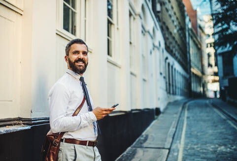 Hipster businessman standing on the street in London, holding smartphone. Copy space. - HPIF30004