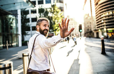 Rear view of hipster businessman walking up the street in London, looking back and greeting somebody. Copy space. - HPIF30008