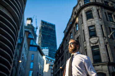 Low angle view of hipster businessman with sunglasses standing on the street in London city. copy space. - HPIF30009