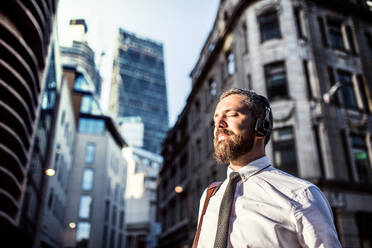 Hipster businessman with headphones standing on the street in London city, listening to music. Copy space. - HPIF30011