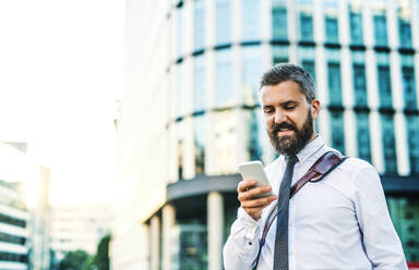 Ein Porträt von Geschäftsmann mit Smartphone stehen auf der Straße in der Stadt vor einem Gebäude, Text-Messaging. - HPIF30013