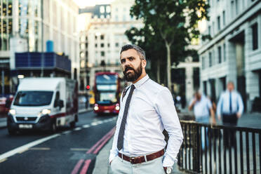 Hipster businessman standing on the street in London next to a busy road, hands in pockets. - HPIF30017