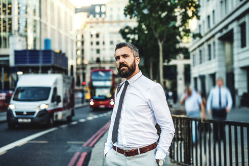 Hipster-Geschäftsmann auf der Straße in London neben einer belebten Straße, die Hände in den Taschen. - HPIF30017