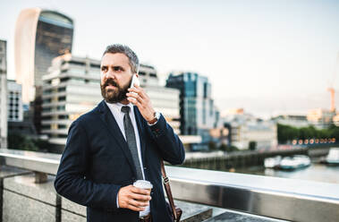 Serious hipster with businessman with coffee and smartphone standing outdoors in the city, making a phone call. - HPIF30046