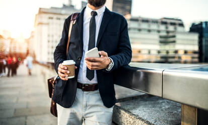 Unrecognizable businessman with smartphone and coffee standing on the bridge in London. - HPIF30048