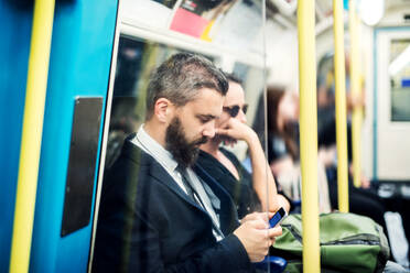 Hipster Geschäftsmann mit Smartphone sitzt in der U-Bahn in der Stadt, auf dem Weg zur Arbeit. - HPIF30051