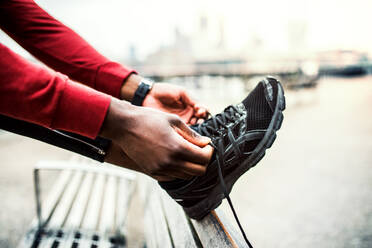 A close-up of an unrecognizable young sporty black man runner tying shoelaces before running outside in a city. - HPIF30073