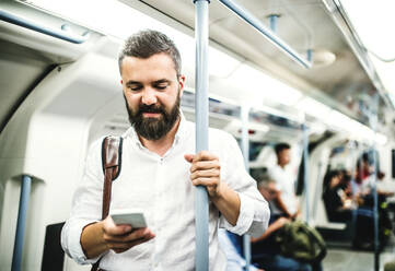 Hipster-Geschäftsmann mit Smartphone steht in der U-Bahn in der Stadt, auf dem Weg zur Arbeit und SMS schreiben. - HPIF30075