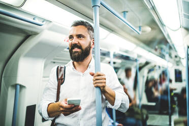 Hipster-Geschäftsmann mit Smartphone steht in der U-Bahn in der Stadt, auf dem Weg zur Arbeit und SMS schreiben. - HPIF30076