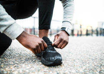 A close-up of an unrecognizable young sporty black man runner tying shoelaces before running outside in a city. - HPIF30093