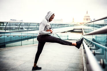 Junge sportliche schwarzer Mann Läufer Stretching auf der Brücke in einer Stadt, Einstellung Smartwatch. - HPIF30100